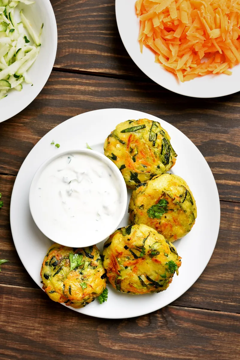 Gemüselaibchen mit Dip, daneben geraspelte Karotten und Zucchini
