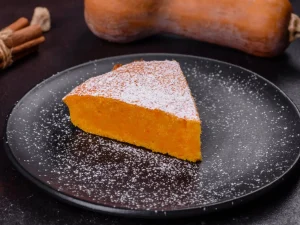 Stück Kürbis-Kuchen mit Staubzucker auf einem dunklen Teller